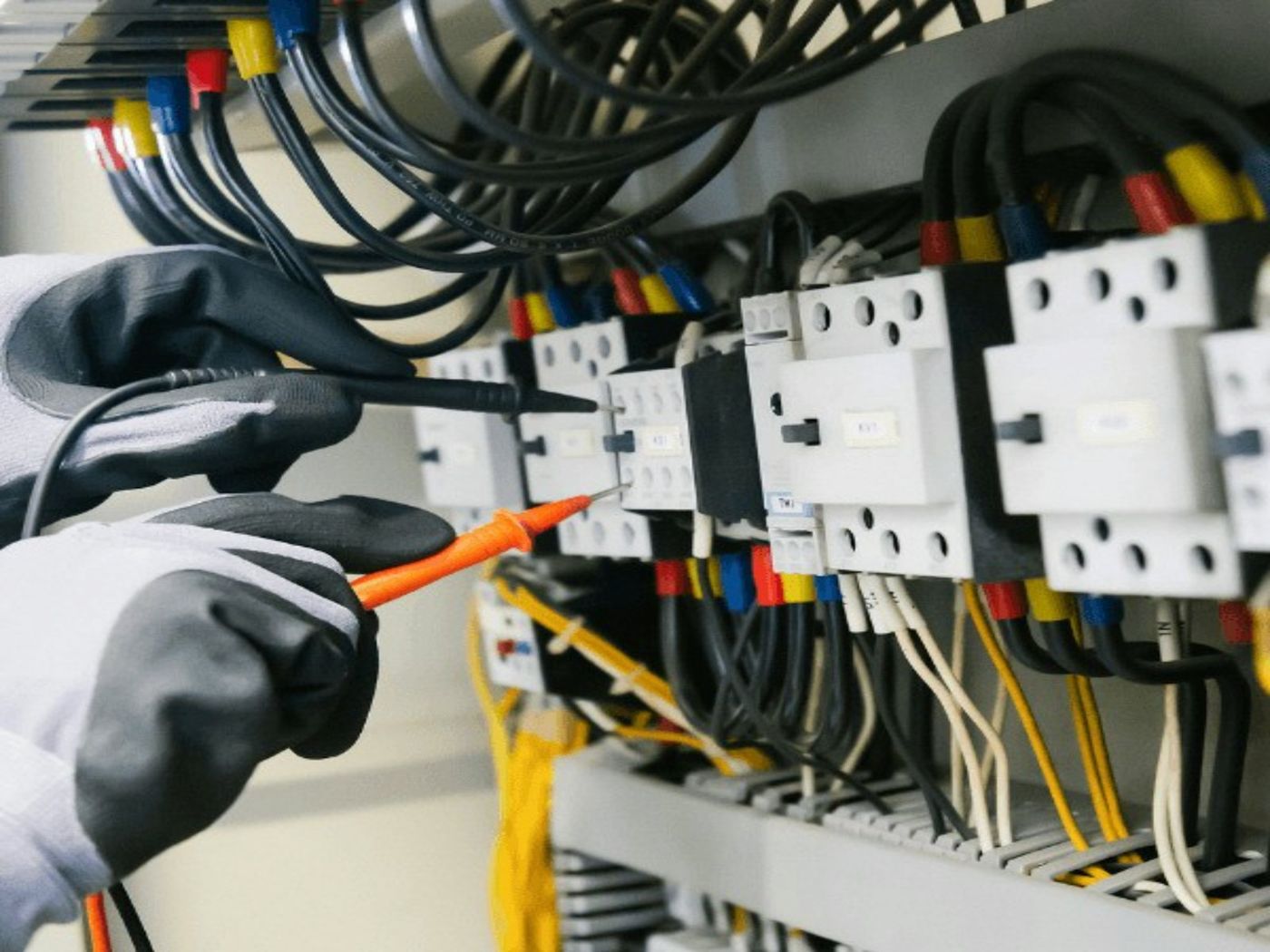 A gloved electrician testing wires in a switchboard
