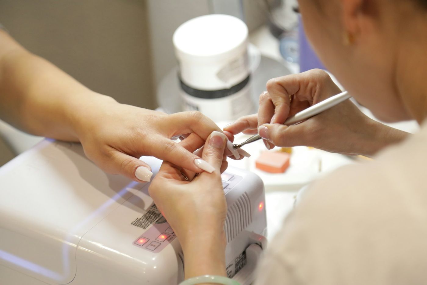 A nail technician painting a client's nails next to a UV lamp