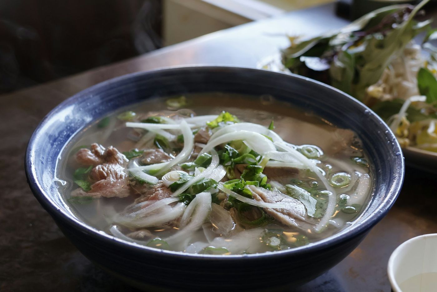 A bowl of beef phở with sliced onion and spring onion